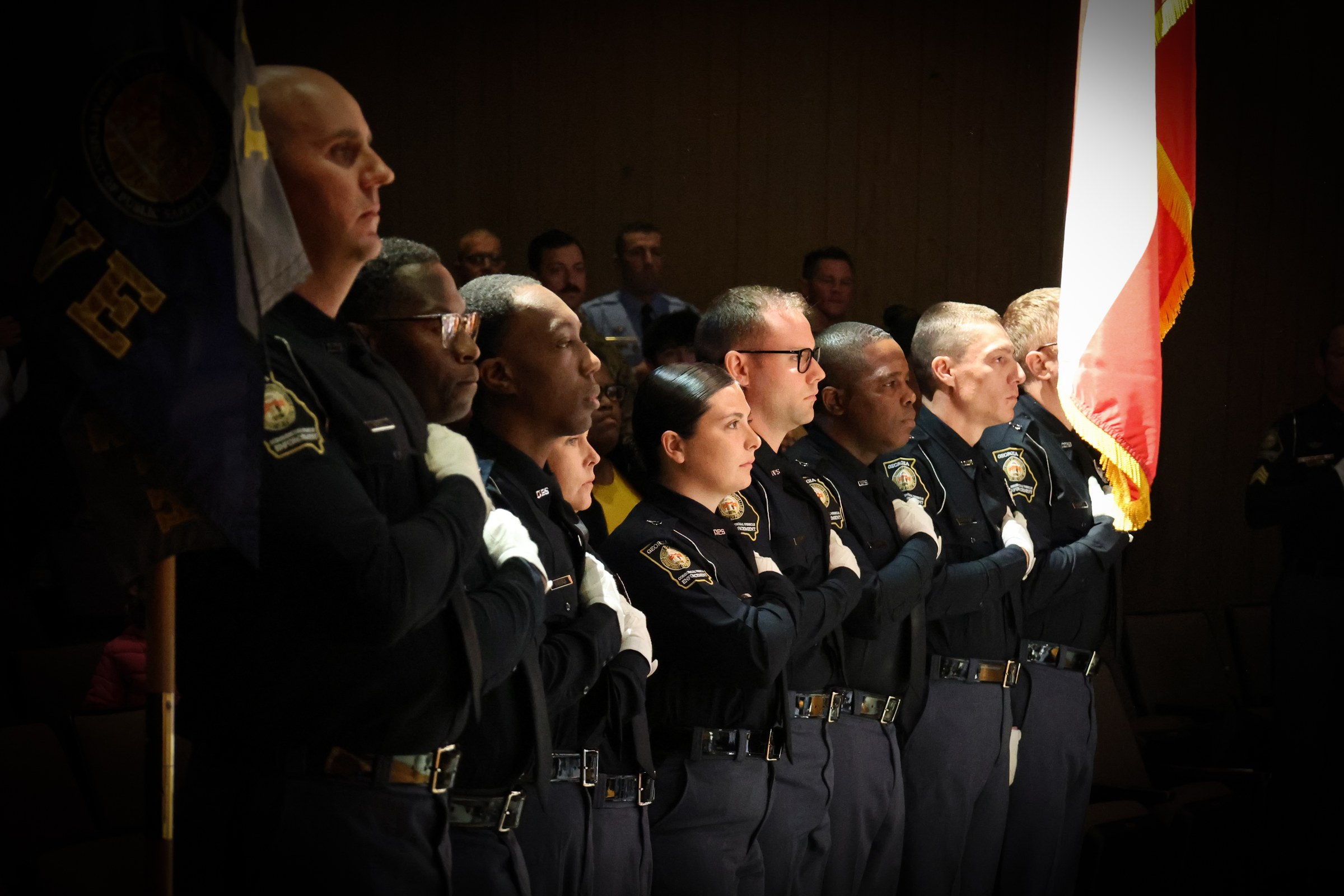 Row of CVE officers in dress uniform standing at attention beside the flag during a graduation ceremony